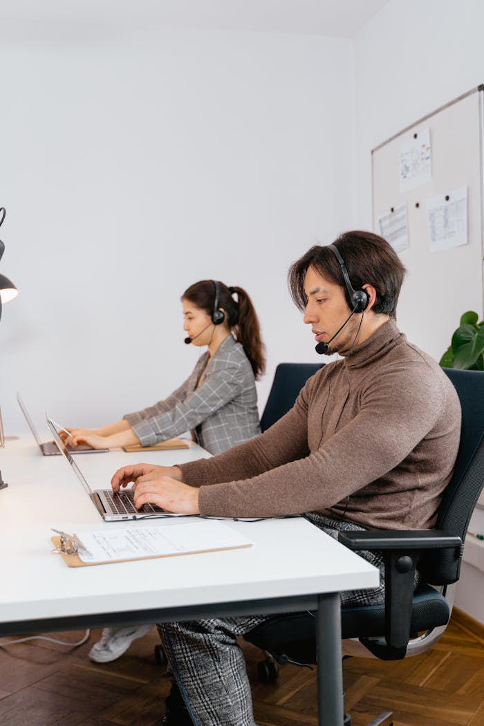 Colleagues with headsets working in a modern office environment, focused on laptops and collaboration.