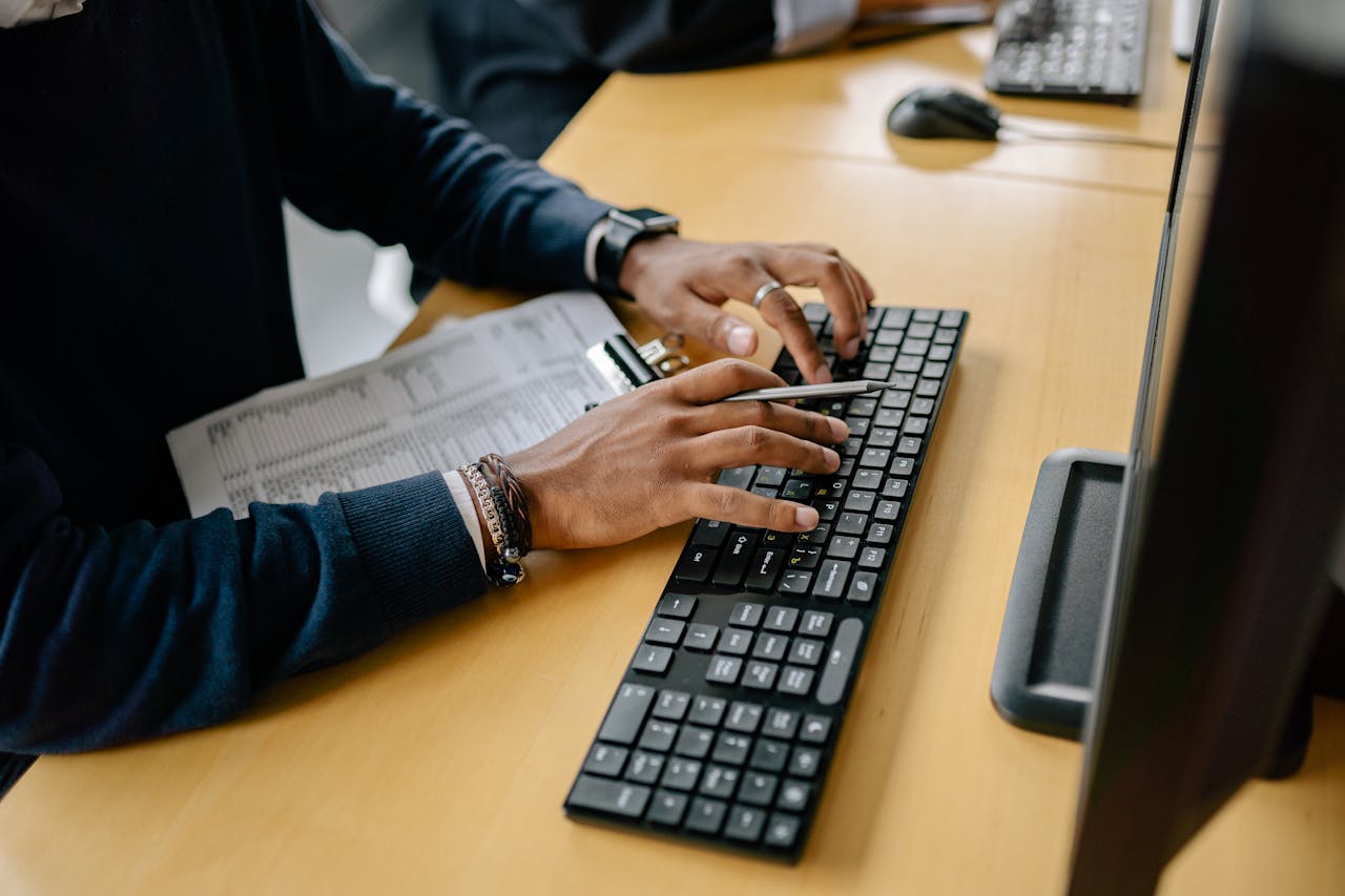 Close-up of hands typing on a keyboard in an office setting with clipboard nearby.